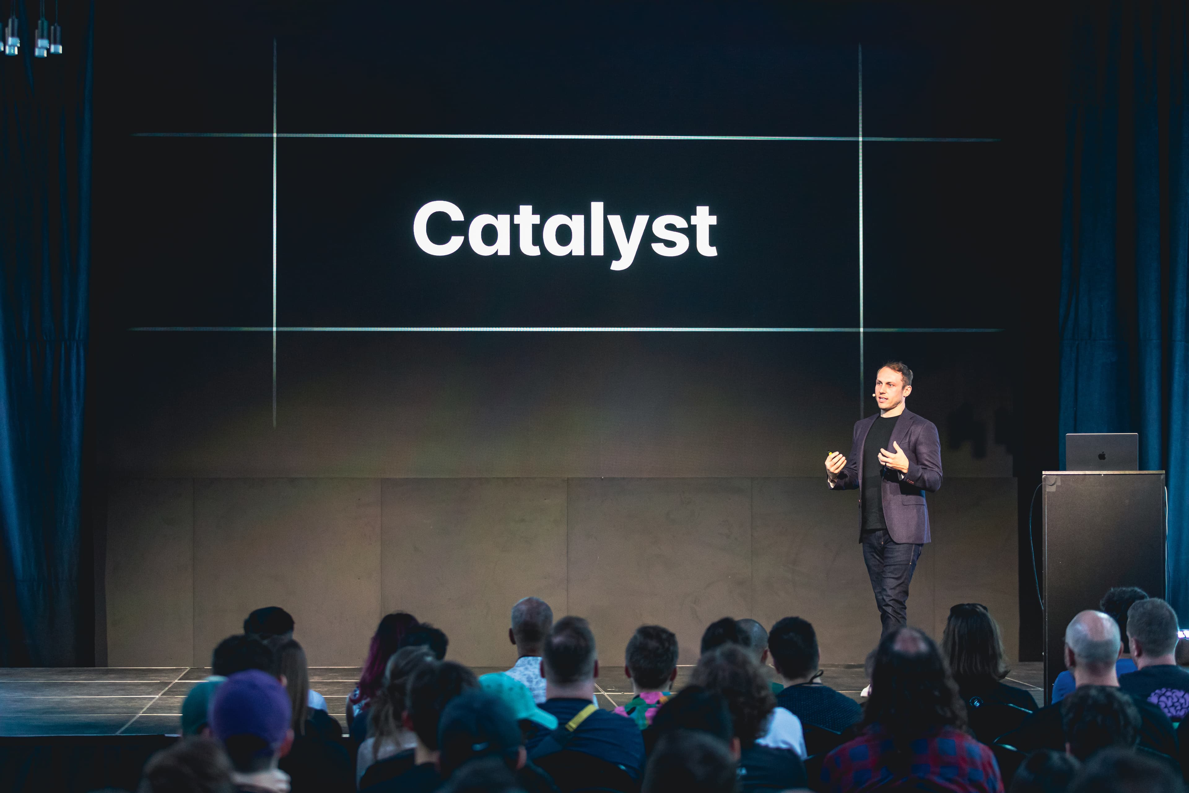 Adam Wathan 站在舞台上，面前有一张写着 Catalyst 的幻灯片