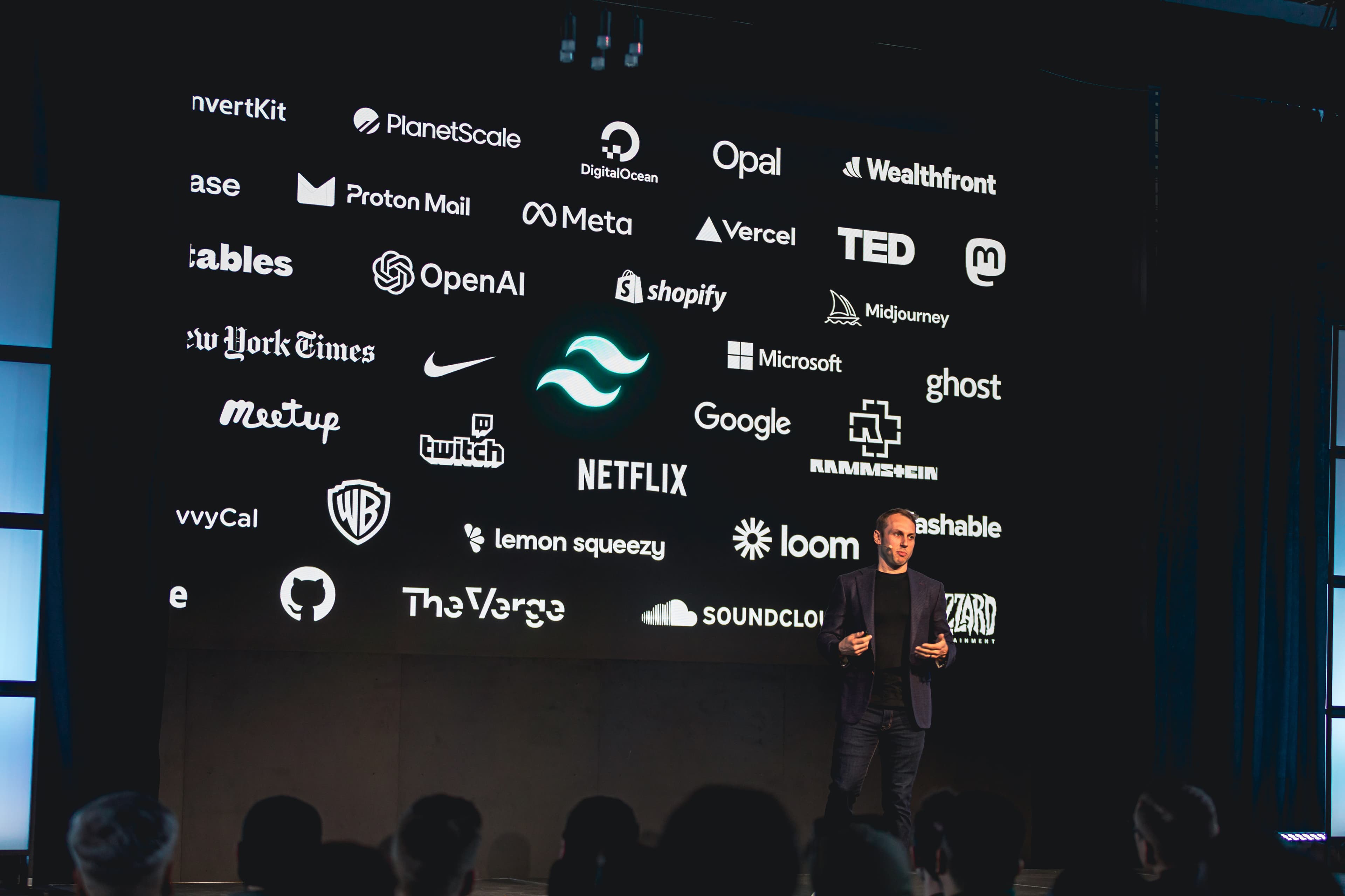 Adam Wathan 站在舞台上，讲解一些使用 Tailwind CSS 的公司