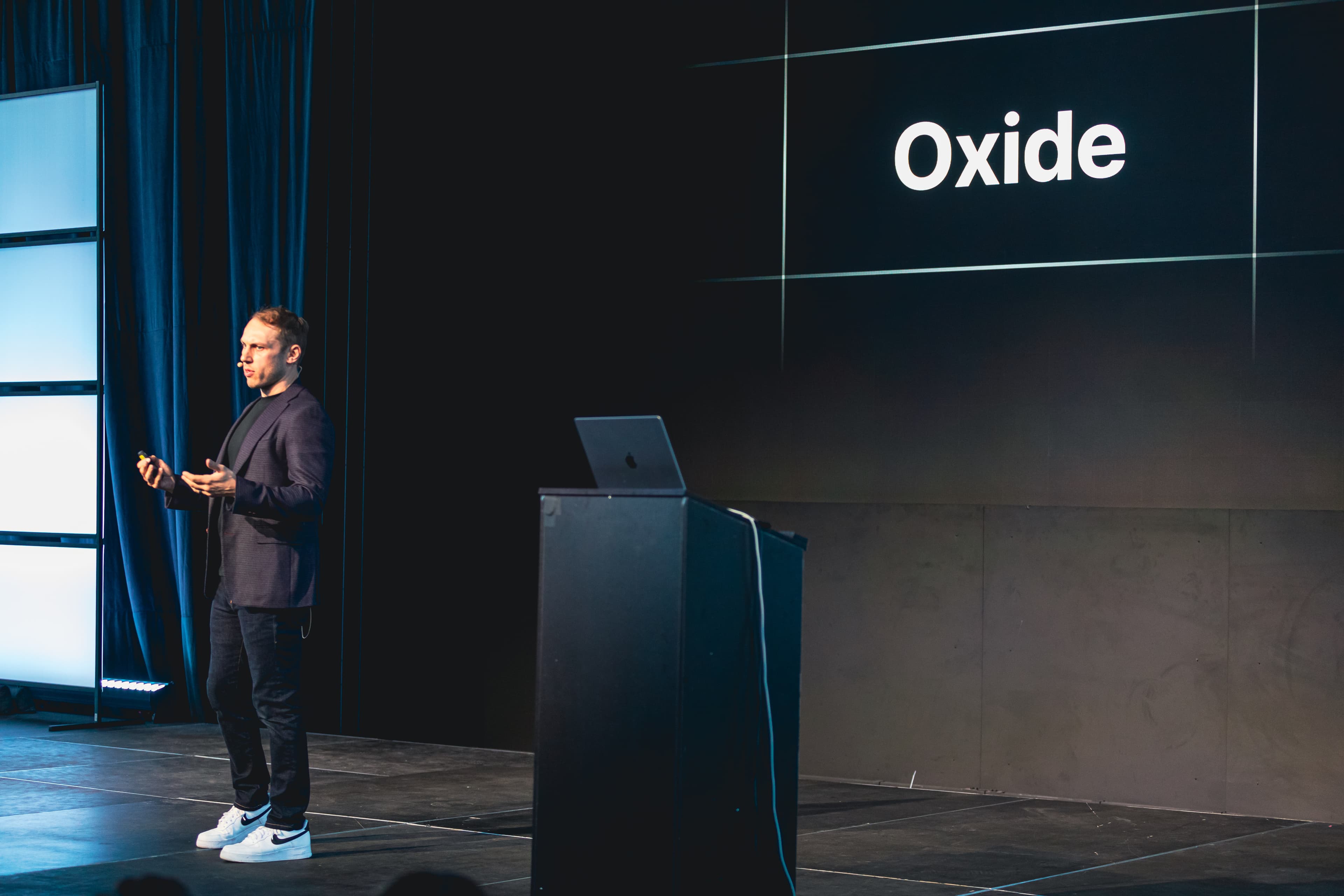 Adam Wathan 站在舞台上，面前有一张写着 Oxide 的幻灯片